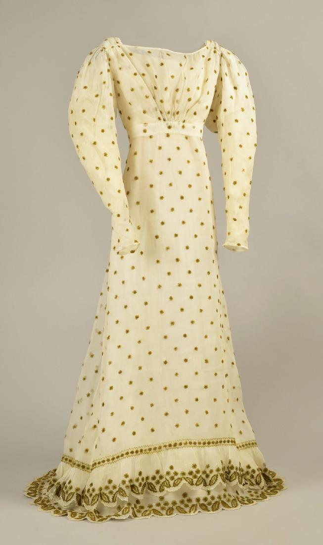 WOOL EMBROIDERED MULL DRESS, c. 1824: White cotton sprigged with olive green wool star embroidery having high waist bodice with long gigot sleeve, ruched at center front having wide waistband, back closure with six embroidered buttons and