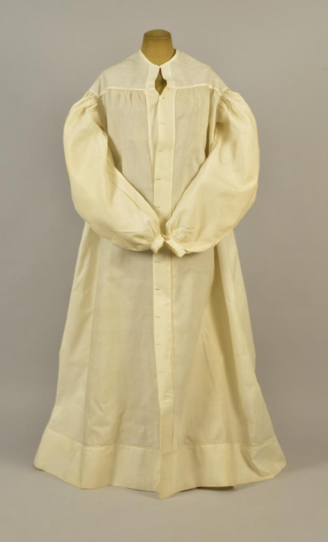 WHITE COTTON MUSLIN DRESSING GOWN, 1830: Long sleeve puffed at the shoulder and gathered into narrow cuff with embroidered button, yoke and shoulder having self piping, front button placket, back gathered into yoke and waistband, wide hem ba