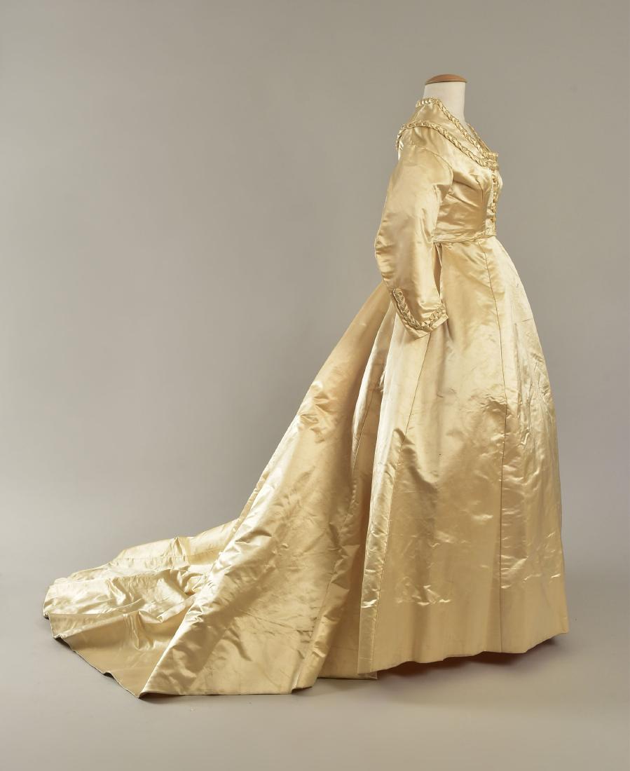TRAINED SATIN WEDDING GOWN with BRAIDED TRIM, 1867: 2-piece ivory silk, bodice having squared neckline and long sleeve, trimmed with self braiding, crocheted buttons, cotton lining; skirt having plain front and pleated back with long, curved train, sti