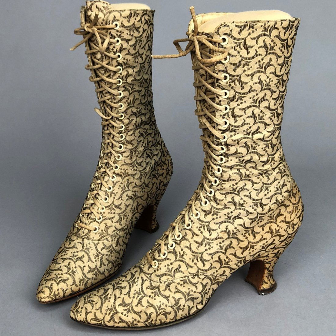 METALLIC BROCADE LACE-UP BOOTS, c. 1895: Cream canvas having allover metallic silver embroidery in a foliate pattern. Label "Thayer McNeil Company Boston". 10 x 11 with 2 3/4-inch heel. Includes custom mount. (Slight darkening of canvas, soi