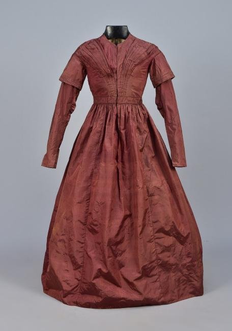 BROWN SILK DRESS, AMERICAN, c. 1840: Chestnut taffeta with a subtle woven stripe having long collared sleeve with tucks, shaped with small gathers at the elbow, bodice front with fan pleats lined in glazed muslin padded at the bust, wais