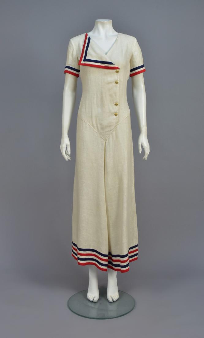 PATRIOTIC LINEN COULOTTE JUMPSUIT, 1940s: Short sleeve white linen having off-center closure with brass anchor buttons below a single wide lapel trimmed in red and blue linen bands, ankle-length split skirt set in a deep point with four color