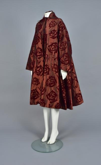 ROMEO GIGLI RUNWAY ASIAN-INSPIRED SWING COAT, 2002: Runway finale look in wine-colored dull satin flocked with abstract Asian symbols, wide pointed collar, raglan sleeve, hidden button placket with a single poured glass button with copper spiral at the