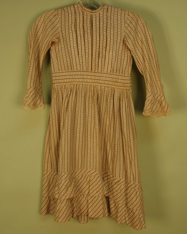 YOUNG GIRL'S PRINTED COTTON CALICO DRESS, 1870's. : YOUNG GIRL'S PRINTED COTTON CALICO DRESS, 1870's. Long sleeve in cream having a tiny vertical repeat in red alternating with brown, pleated bodice, wide waistband, skirt having two banded hem ruffles,