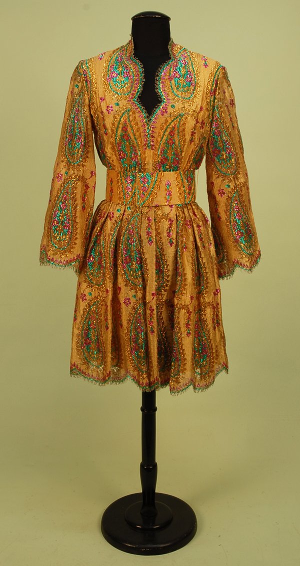 BLASS FOR RENTNER METALLIC LACE PAISLEY DRESS, 196: BLASS FOR RENTNER METALLIC LACE PAISLEY DRESS, 1960's. Short dress having long sleeve and full skirt with scalloped hem and neckline, wide self belt, in gold metallic lace with large fuchsia, green an