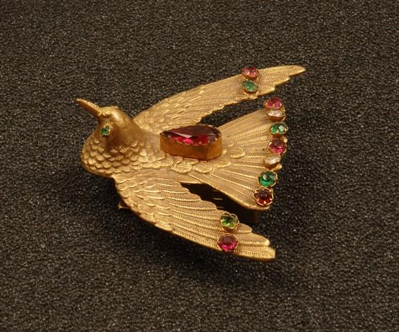 ENGLISH VICTORIAN BIRD FORM NEEDLE CASE. Gilt met: ENGLISH VICTORIAN BIRD FORM NEEDLE CASE. Gilt metal casting of a spread winged bird in fine detail with arcade set colored stones mounted above a rectangular box with separate lid, bottom stamped "W.