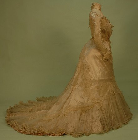 TRAINED CREAM SILK and LACE EVENING GOWN, 1890's: 2-piece, the high neck boned bodice having tucked chiffon, unusual lace applique to yoke and long sleeve, full satin skirt with pleated hem flounce having chiffon overlay with lace applique falling to