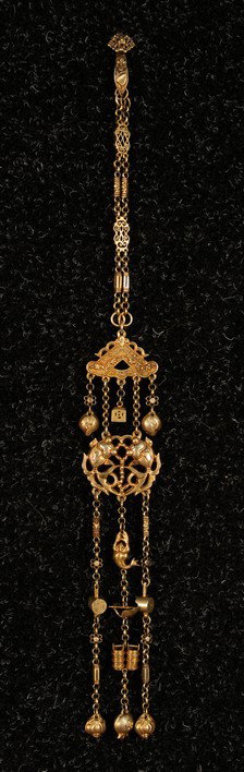 VICTORIAN BRASS CHATELAINE. Composed of large swim: VICTORIAN BRASS CHATELAINE. Composed of large swimming fish medallion and various Chinese objects, fruits and symbols. Length 16. Excellent.