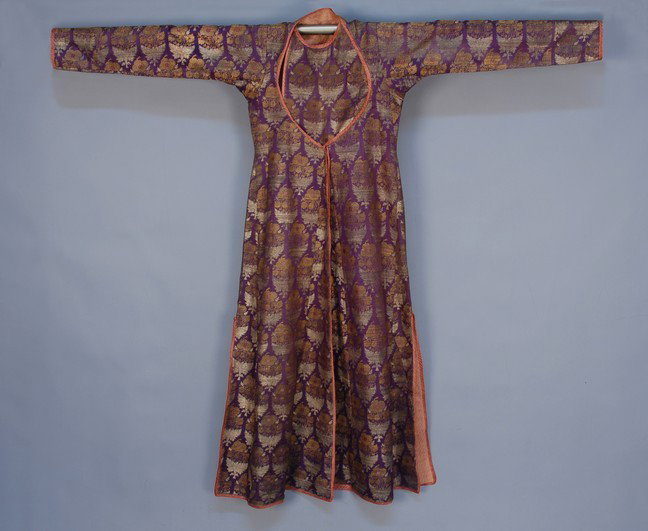 INDIAN METALLIC BROCADE SILK LONG COAT, c. 1885. P: INDIAN METALLIC BROCADE SILK LONG COAT, c. 1885. Purple silk having a repeat of stylized floral bouquets in rose silk, gold and silver metallic brocade, with inset bib having button and tie closure, t