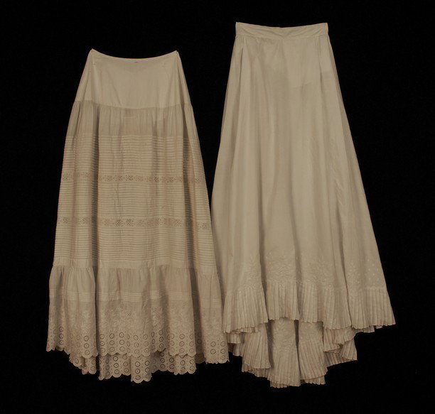 TWO WHITE COTTON PETTICOATS, 1869 and LATE 19th C.: TWO WHITE COTTON PETTICOATS, 1869 and LATE 19th C. The earlier trained and having knife pleated hem ruffle below a band of white embroidered floral devices on an oval repeat, W-26, L 39-49. The later 