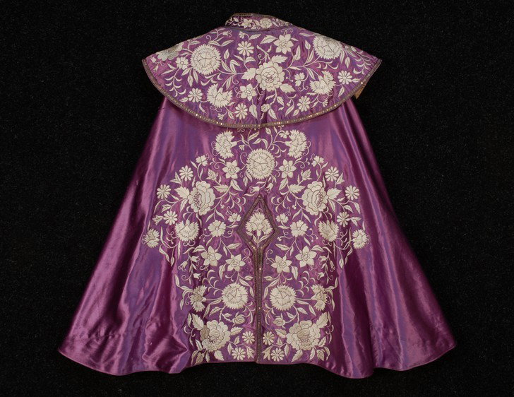 CHINESE EXPORT EMBROIDERED and SEQUINNED CAPE, c. : CHINESE EXPORT EMBROIDERED and SEQUINNED CAPE, c. 1930. Short cape with shawl and stand collars, made for the Spanish market in lilac silk satin, having white satin stitch floral decoration with narro