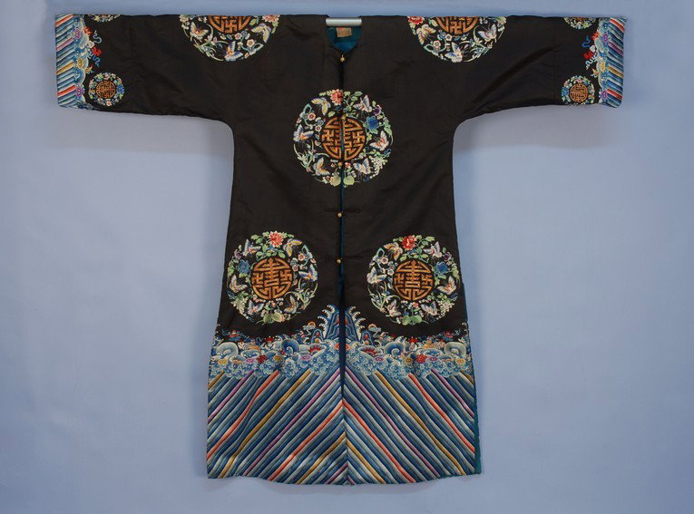 CHINESE EXPORT EMBROIDERED SILK LONG COAT, MID 20t: CHINESE EXPORT EMBROIDERED SILK LONG COAT, MID 20th C. Floor length black satin with couched metallic gold medallions within a butterfly and flower border, deep wave and rainbow hem border slit in bac