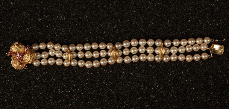 14K GOLD, PEARL and RUBY BRACELET, 20th C. Three s: 14K GOLD, PEARL and RUBY BRACELET, 20th C. Three strands of 5.8 mm pearls (72 total), every six pearls separated by leaf form gold collar, having 14K gold, ruby and tiny diamond trefoil clasp. 6 1/2 x