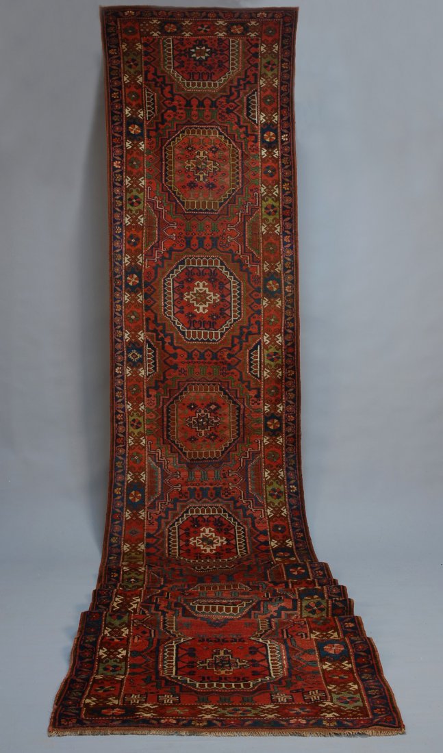 AFGHAN BASHIR, EARLY 20th C. Long runner in red, b: AFGHAN BASHIR, EARLY 20th C. Long runner in red, blue, yellow and green, twelve octagonal guls surrounded by symetrical geometric elements, full pile, 22 feet 3 inches x 3 feet 3 inches. Excellent.