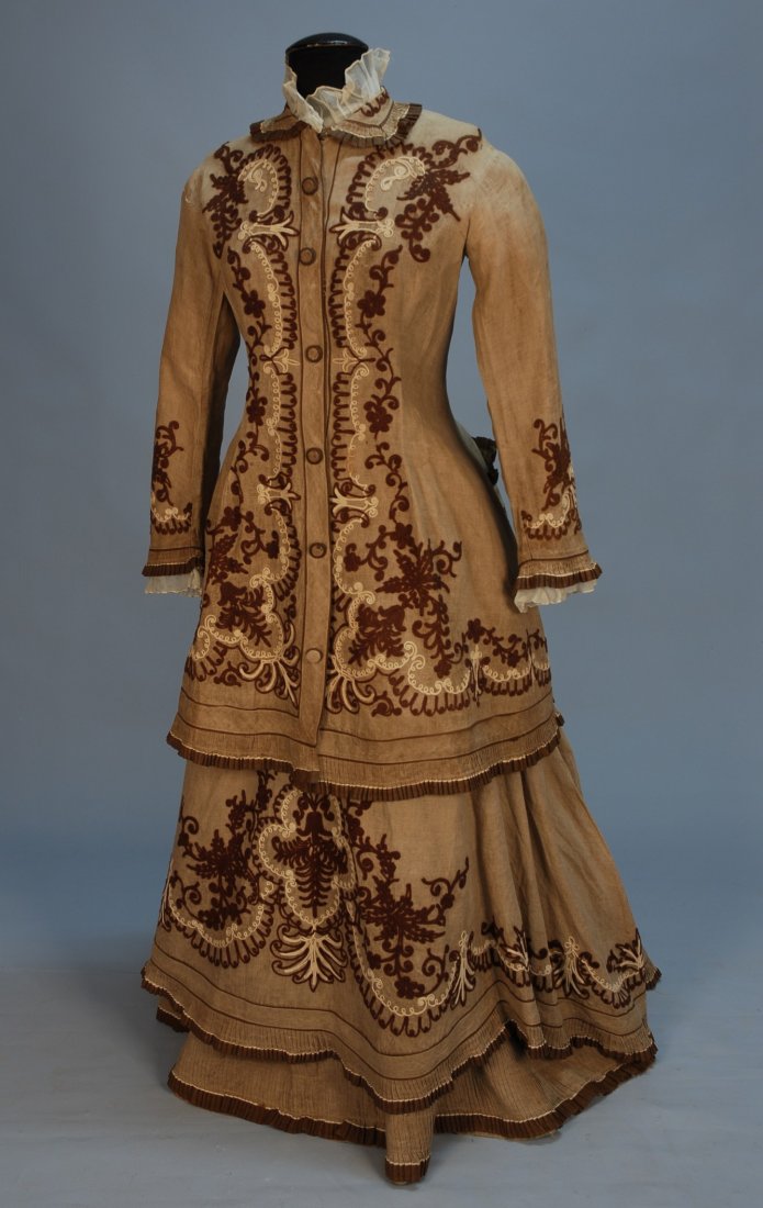 UNUSUAL EMBROIDERED LINEN BUSTLE DRESS, 1870's. 3-: UNUSUAL EMBROIDERED LINEN BUSTLE DRESS, 1870's. 3-piece tan linen with lavish tambour decoration in brown and white wool, trimmed with pleated ruffles having brown and white border, jacket with faux s