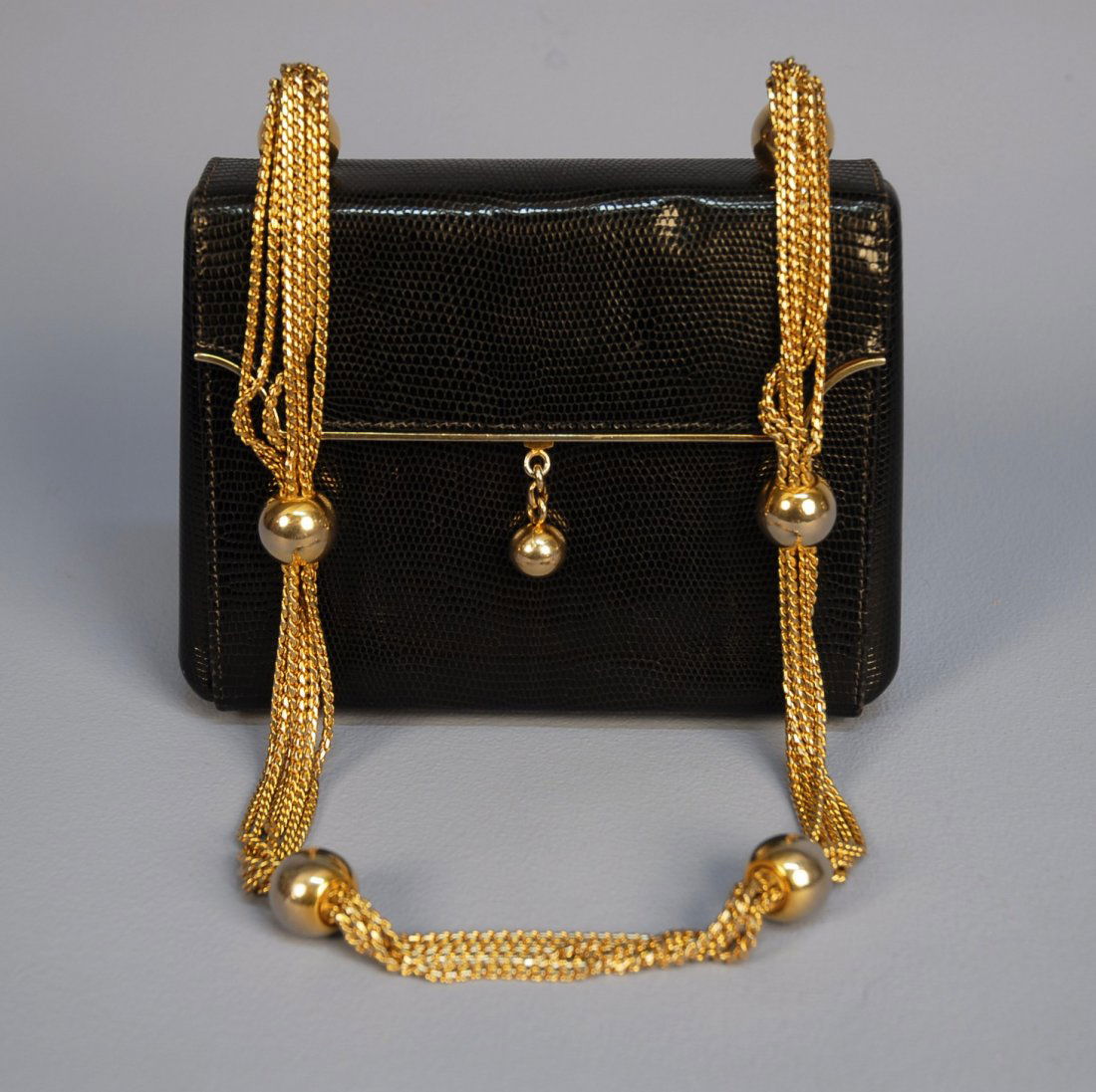 MARK CROSS LIZARD HANDBAG, c. 1970. Black with hea: MARK CROSS LIZARD HANDBAG, c. 1970. Black with heavy brass handle comprised of six fancy link chains and six ball spacers and mounts, fold back top with curve cut corners edged in brass with ball and