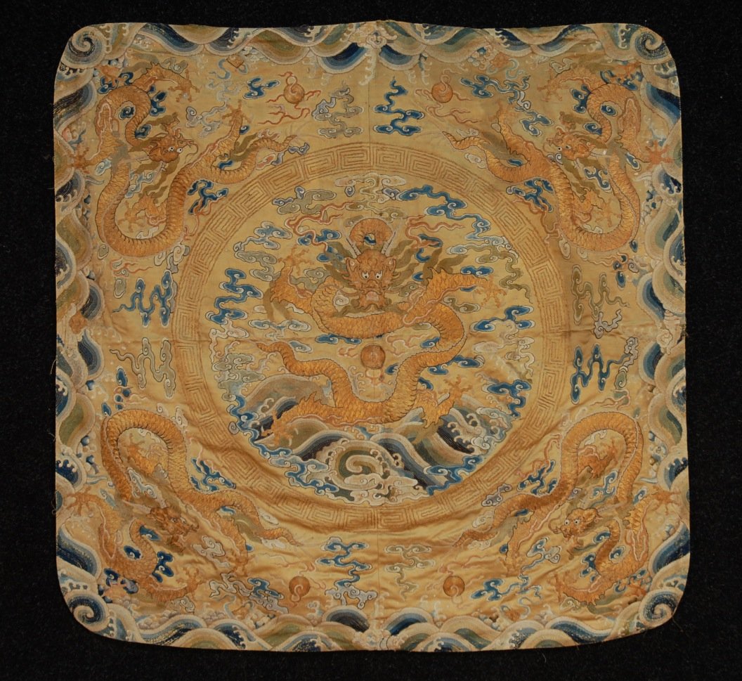 CHINESE EMBROIDERED CUSHION COVER, 19th C.: Gold silk satin square ground decorated with central roundel of large dragon worked in gold metallic thread, the dragon upon silk satin stitch waves and cloud bands all within a Greek key couched meta