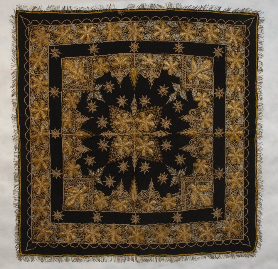 METALLIC EMBROIDERED WOOL SQUARE, EARLY 20th C.: Probably Syrian or Indian, black wool having a stylized floral in padded gold metallic threads, with tambor and couched gold scrolling foliage with white silk details, metallic fringed border. 33 x 32