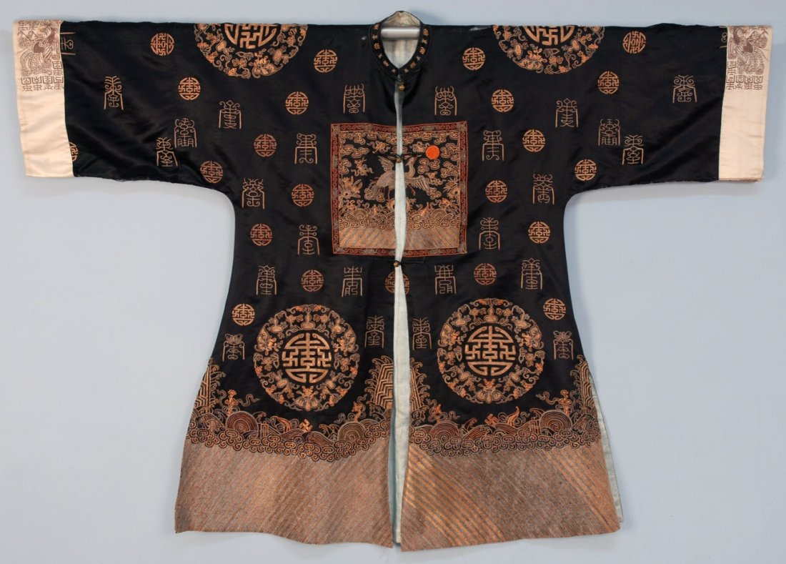 CHINESE SILK EMBROIDERED SURCOAT with RANK BADGES,: Black satin with couched metallic embroidery having fifth civil rank badge with coral beaded sun amid symbols and medallions, white sleeve bands with dragon and bird, li shui border, brass button and 