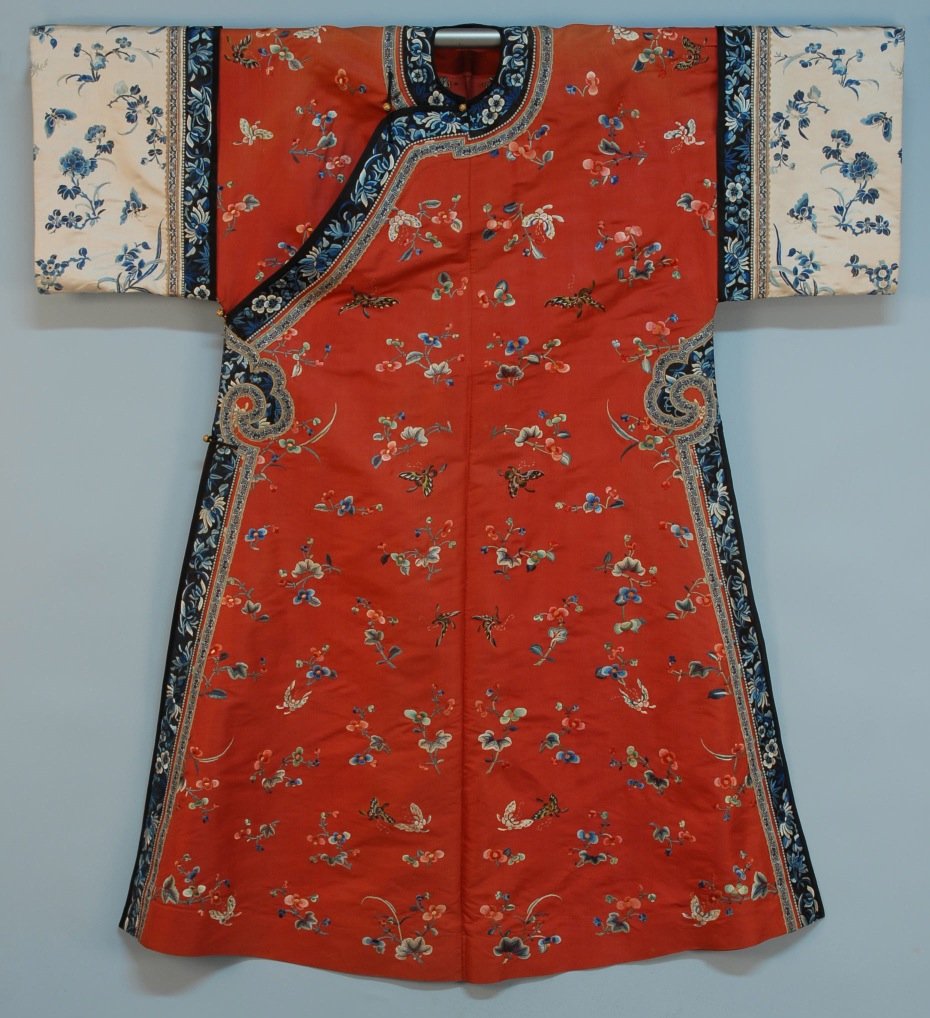 CHINESE SILK EMBROIDERED ROBE, 19th C.: Cinnabar silk with satin stitch embroidered flowers and butterflies with black and white trim bands having blue embroidery and brocade ribbon bands, four brass ball & silk loop closures. 48 x 55. (Ver