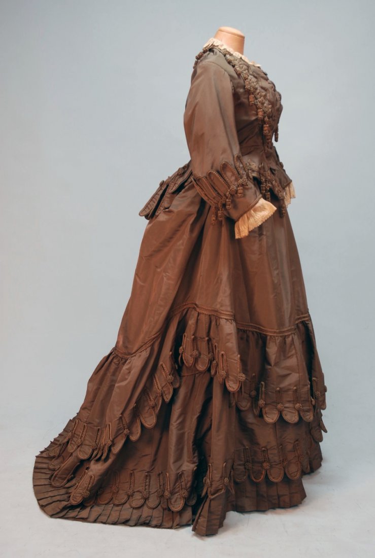 PARIS LABEL SILK AFTERNOON GOWN, c. 1880.: 3-piece mushroom silk faille elaborately decorated with scallops, braiding and tassels, semi-boned peplum bodice with self buttons and lace trim, trained skirt having deep hem ruffle above pleats with