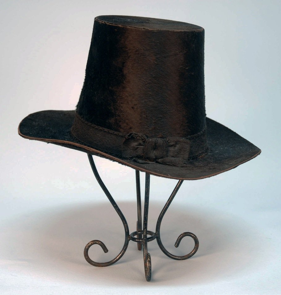GENT'S BROWN BEAVER TOP HAT, 1830's.: Flower pot shape with wide flat brim, having woven floral band, quilted cotton twill sweatband, paper crown lining with maker's emblem. 14 1/2 x 13 x 6 3/4 inches high. SM. (Wear to edge of crown and 