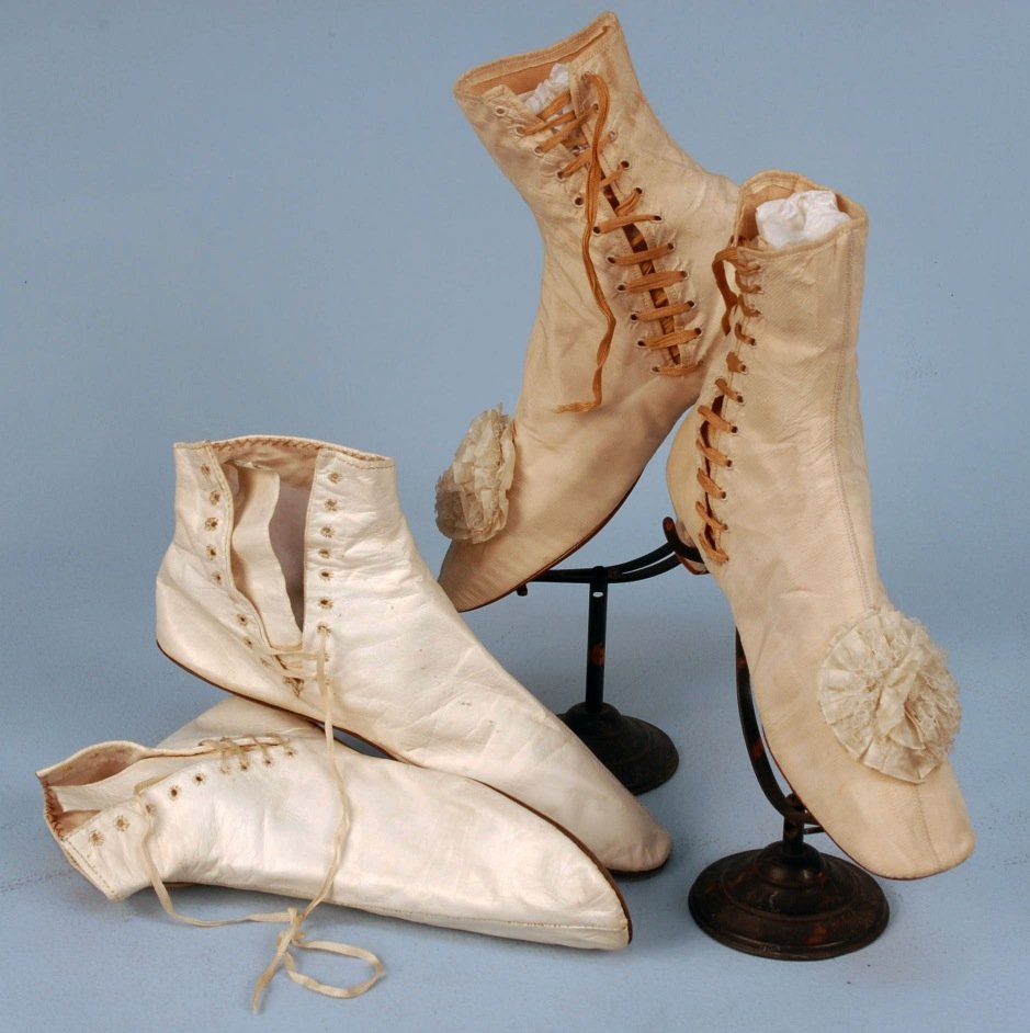 TWO PAIR LADIES' SHOES, 1830's-1850's.: One pair side lacing white kid short boots, straights and flats. One pair striped ivory silk side lace boots with small Louis heel and ribbon and lace rosettes on vamps. (Slight wear and spots) very g