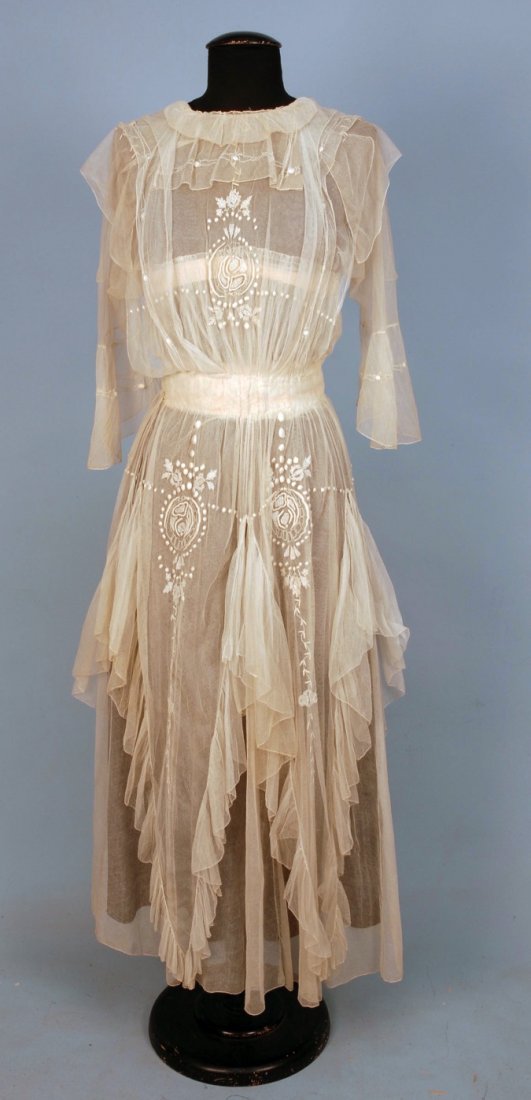EMBROIDERED NET TEA GOWN, EARLY 20th C.: Fine cream net with square collar and flared elbow length sleeve having an overskirt with four long ruffled points, embroidered with a stylized floral, V-back and back closure. B-34, W-24, L-52. SM. (