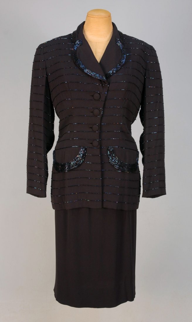 HOWARD GREER BEADED CREPE COCKTAIL SUIT, 1949.: Navy blue with long jacket having horizontal bands of blue iridill bugle beads, rounded collar, lapel and double flap faux pockets all edged with wide band of beads, self buttons and crepe lining. Nar