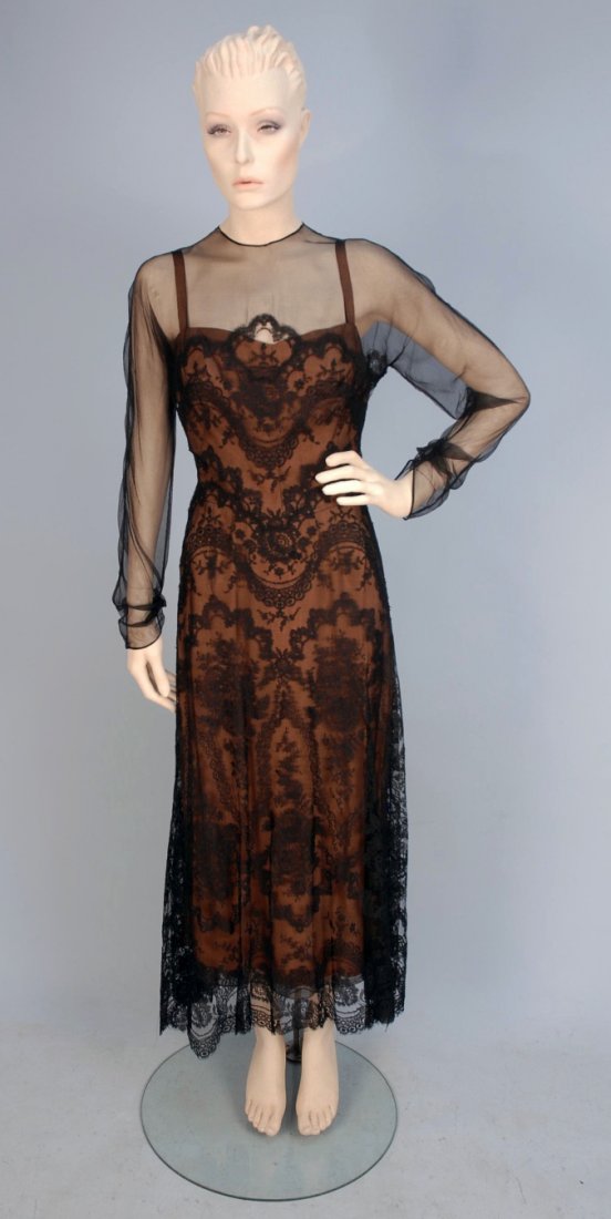 IRENE BLACK LACE COCKTAIL DRESS, c. 1950.: Long sleeve with sheer net bodice top and sleeve with black lace on net over nude crepe underdress having narrow strap, back of skirt trimmed with four velvet bows, back button and loop closures over 