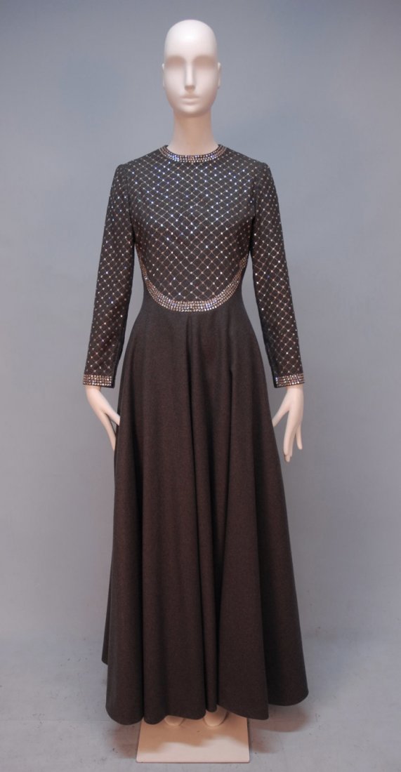 GEOFFREY BEENE JEWELED WOOL EVENING DRESS, c. 1970: Long sleeve felted grey wool with jewel neck, curved waist and cuff decorated with a band of prong set rhinestones, bodice having a metallic stitched diamond lattice jewel studded at corners, full ski