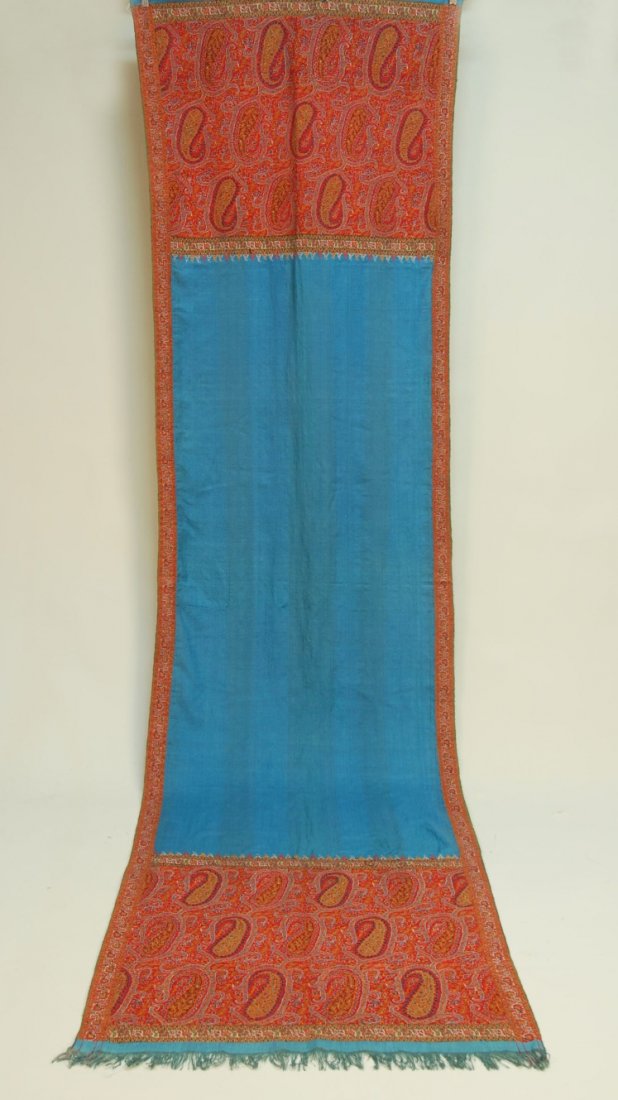 HANDMADE KASHMIR PAISLEY SHAWL, 19th C.: Long blue wool open field with brightly colored paisley border, deep end borders with embroidered edge. 29 1/2 x 108. (4 inch repaired "L" shaped tear) good. SM.