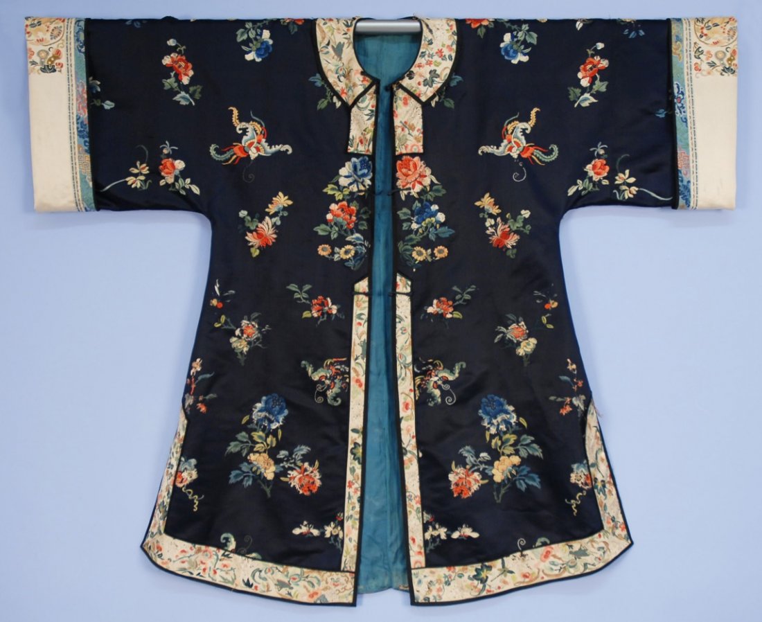 CHINESE SILK EMBROIDERED SURCOAT, EARLY 20th C.: Midnight blue satin decorated with flowers, butterflies and bats in colorful silk satin stitch, neck and hem banded in in ivory satin, sleeves having ivory turn back cuff with brocade ribbon bands and