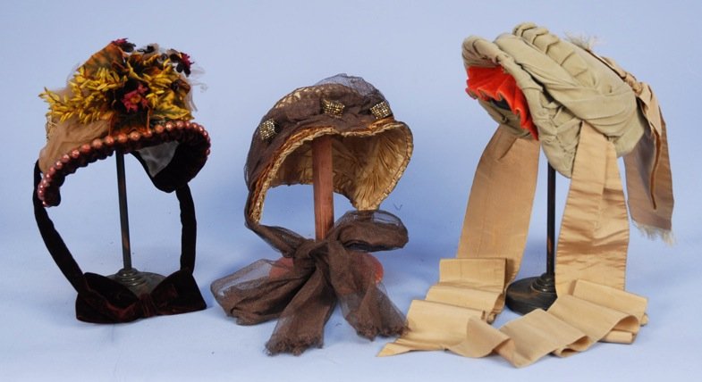 THREE SILK BONNETS, 1880's.: One tan decorated with velvet, straw, metallic cord and cloth flowers, (lining torn). One taupe satin with crochet, straw, net and marcasite cubes, (breaks to straw). One green faille with pleated red
