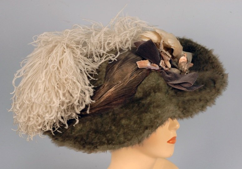 LADY'S WIDE BRIM HAT, 1900-1910.: Sage green plush having crushed crown draped in gold lame, brim turned up to one side and decorated with cloth and silver lame rosebuds, white feathers and brown velvet bow. 14 x 16. (Some losses to f