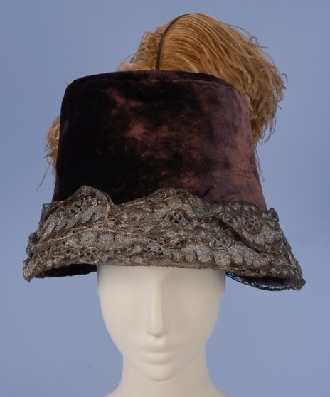 FRENCH VELVET TOQUE with METALLIC LACE, 1912.: Oversized plum velvet trimmed with silver metallic lace around brim having two caramel colored ostrich plumes mounted above back bow. Paris label. 12 x 8. (Minor losses to feathers, relined) excellent