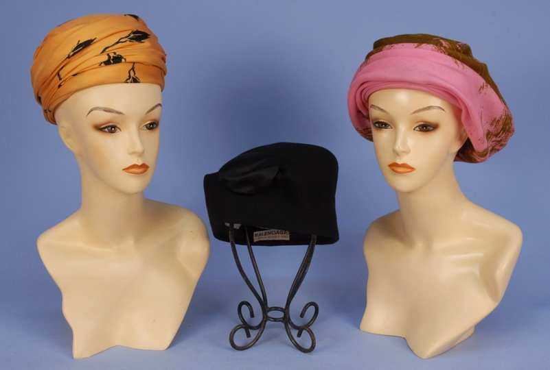 THREE BALENCIAGA HATS, 1960's.: One yellow silk faille turban printed with black rosebuds. One pink and brown printed wool turban with back bow. One asymmetrical black wool felt toque with silk applique. (Small red mark on yellow si