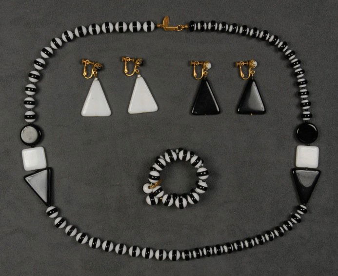 MIRIAM HASKELL DEMI PARURE.: Black and white glass beads in two patterns, necklace having two separators with flat geometric shapes, memory wire bracelet and two pair triangle drop earrings. Signed. Necklace 15 inches. Excellent.