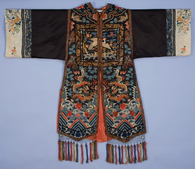 CHINESE SILK EMBROIDERED SURCOAT with RANK BADGES,: Black with metallic gold and silk dragons amid cranes, bats and clouds above li shui border with flowers, cream sleeve bands with squirrels in Peking knot, metallic brocade trim and double pointed fro