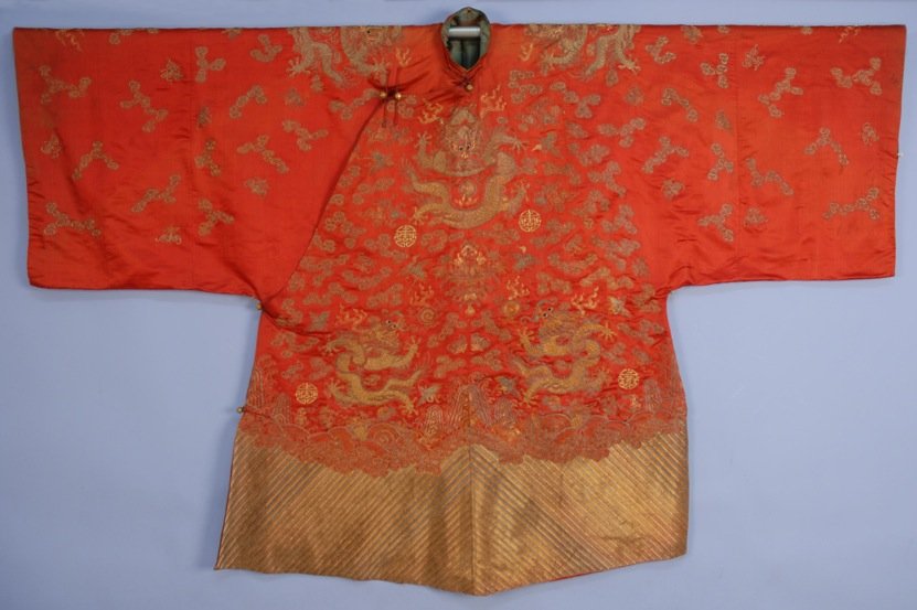 METALLIC EMBROIDERED SILK TEN DRAGON ROBE, LATE 19th C.: Cinnabar satin short robe decorated with couched silver and gold threads having dragons, flaming pearls, clouds, cranes, etc., wide sleeve and li shui border. 70 x 42 1/2. (Some fading, lining stained