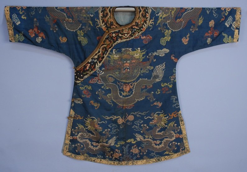 CHINESE SILK BROCADE ROBE, c. 1930.: Blue with dragons, flaming pearls, bats and flowers, neckline trimmed with embroidered black band, sleeve and hem bound with embroidered ivory satin. 52 x 37. (Wear to trim, some thread losses) good. 