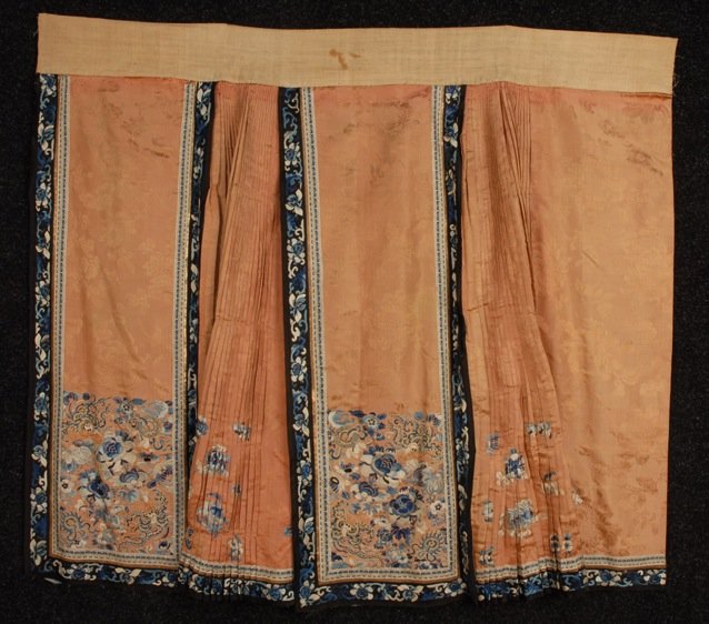 CHINESE SILK EMBROIDERED WEDDING SKIRT, EARLY 20th C.: Salmon damask decorated with satin stitch and Peking knot embroidery in shades of blue and white with metallic gold threads, trimmed with embroidered black satin and brocade ribbon. 45 x 35 1/2. (Some