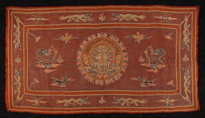 CHINESE EMBROIDERED PANEL, EARLY 20th C.: Red silk with embroidered center roundel of pagoda surrounded by dragons, horses, phoenix birds, etc., all on couched fishnet field. 30 x 54. (Some loose threads) very good.