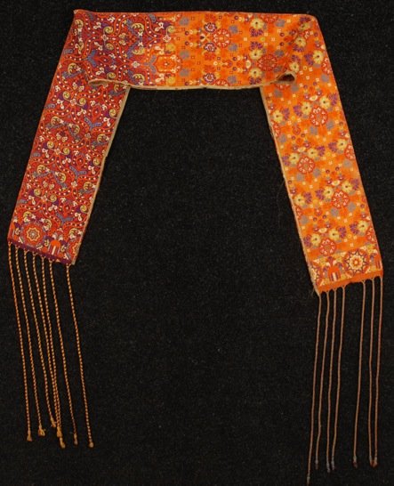 MOROCCAN RAMIE SASH, 19th C.: Polychrome geometric floral design with long braided fringe. 9 x 86 with 23 inch fringe. (Edge wear and minor losses) good. MMA.