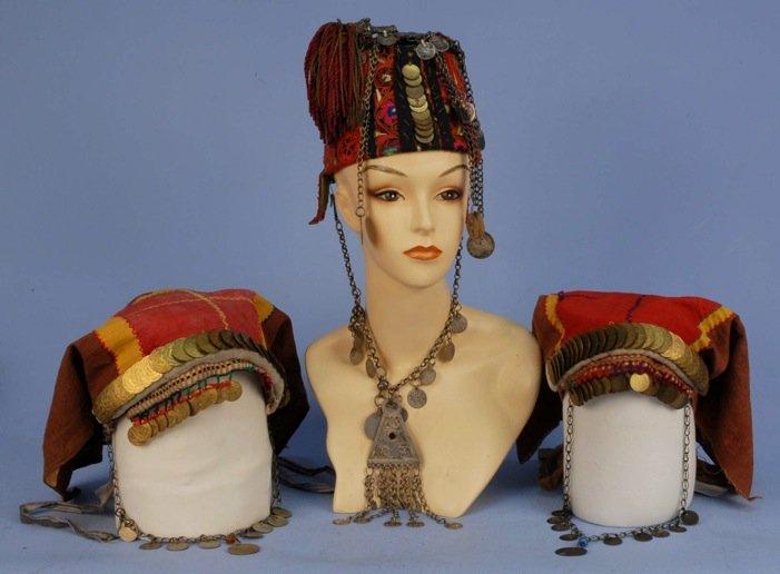 PALESTINIAN HEADDRESS, 19th C.: Red and green felt having polychrome embroidery decorated with beadwork, coins, chains and metallic cap with tassel. (Minor losses, one ear flap broken). Together with two Palestinian pieced cotton he