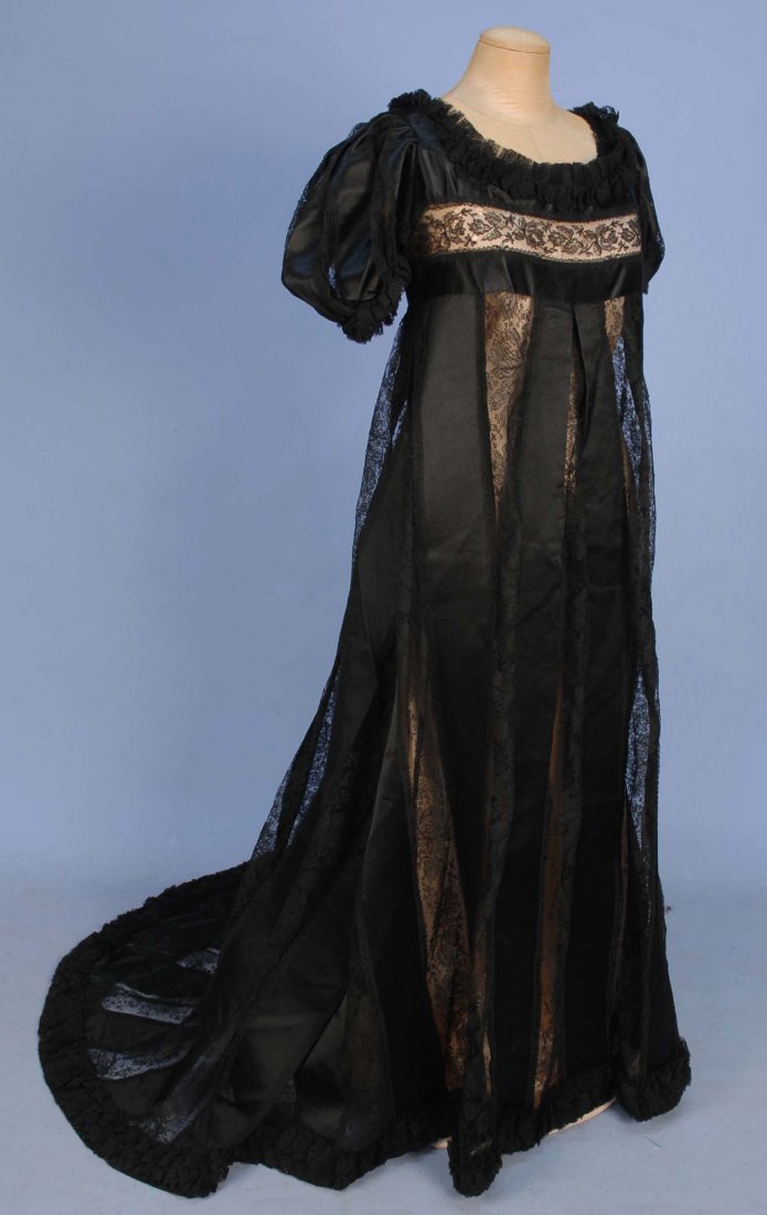 TRAINED SATIN and LACE GOWN, c. 1908.: 1-piece with empire bodice having short puffed sleeve, fashioned from wide black silk ribbon and bands of embroidered net lace, long satin bow at back closure. B-34, high W- 32, front L-55 back L-69. 