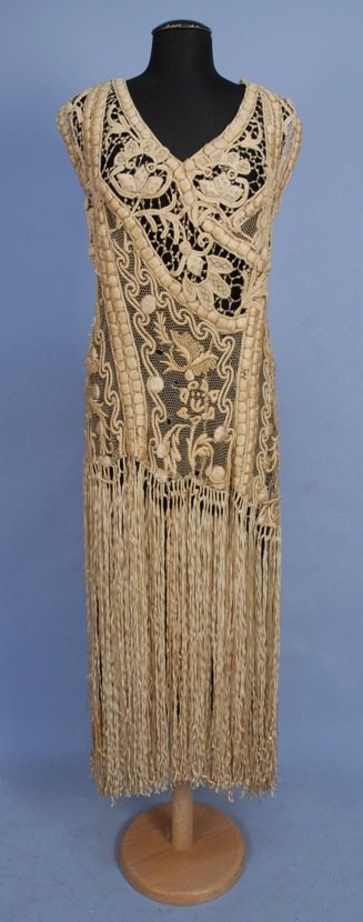 RIBBON EMBROIDERED LACE OVER-DRESS, c. 1920.: Sleeveless ivory net decorated with heavy padded silk embroidery and French knots to below the hip, having a skirt of long ribbon fringe, back closure. B-40, W-34, L-56. (Some breaks to net and brides