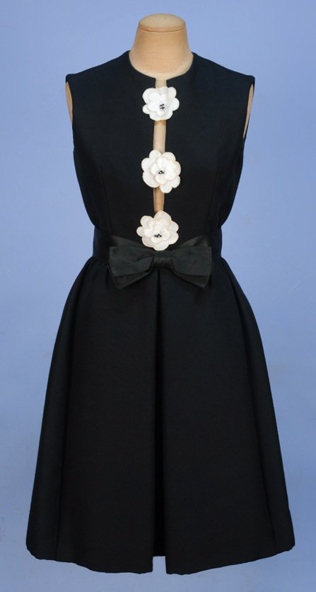 HUBERT LATIMER for IRENE COCKTAIL DRESS, c. 1965.: Sleeveless black wool slashed in front to the waist and appliqued with three white cloth flowers having beaded center, slightly gathered skirt with inverted front pleat and hidden pockets, satin ribbo