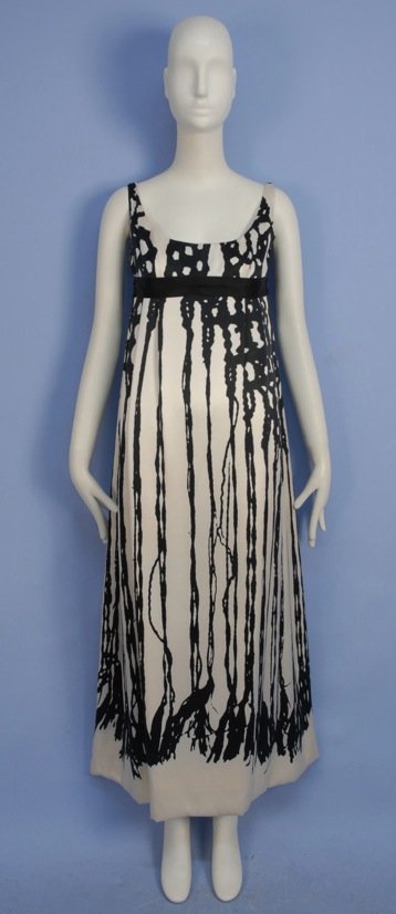 TZAIMS LUKSUS PRINTED SILK EVENING GOWN, 1960's.: Sleeveless white charmeuse printed with stylized macreme and fringe, having empire waist with black ribbon sash, pleated skirt. Labeled. B-34, high W-28, L-53. (Two large water marks, darker stain hid