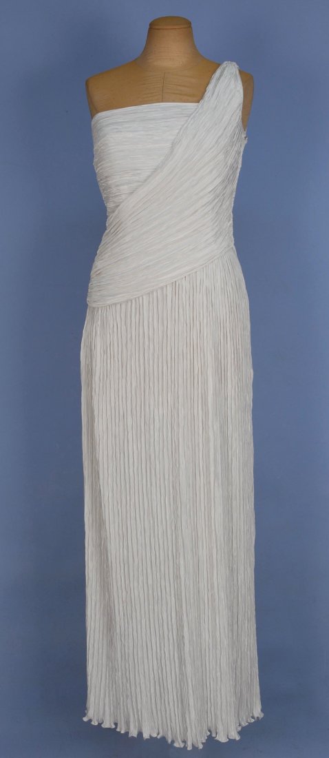MARY McFADDEN ONE SHOULDER-EVENING GOWN, 1980s.: White silk with Delphos style pleats having straight cut neckline and angled swag over one shoulder. Labeled. B-34, W-28, L-58. Excellent.